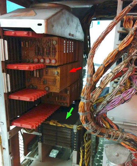Circuitry inside the IBM 1406 Storage Unit. The green arrow indicates the 4,000 character core memory. The cards above it control the memory. The top row of cards has high-current drivers for the memory. The cards in the middle row decode addresses. The bottom row contains amplifiers to read the signals from the memory. The red arrow indicates the position of the faulty card. The fan above the cards provides cooling airflow. At the right, colorful wire bundles connect the circuitry.