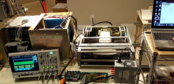 Our test setup to exercise the Diablo disk drive (center) with the FPGA board (front). The oscilloscope shows the sector pulses (top, blue), clock (middle, green), and data (bottom, yellow). Four sectors are visible on the bottom trace. The Xerox Alto is behind the oscilloscope. On the right are the power supply and the laptop controlling the FPGA board.