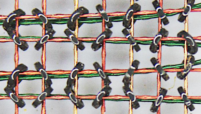 Closeup of an IBM 360 Model 50 core plane. There are three wires through each core. The X and Y wires select one core from the grid. The green wire is the sense/inhibit line.  These cores are 30 mils in diameter (.8mm).