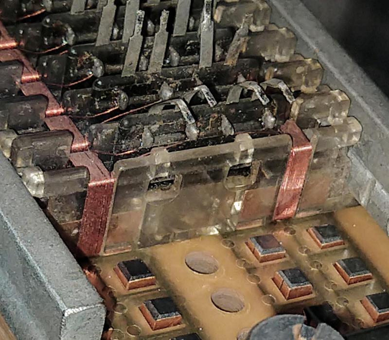 The sense windings are wrapped around the I-bars and connected to pins. The I-bars at the bottom are removed, showing the tops of the transformer U-pieces sticking up through the Mylar tapes. This TROS module is in the Computer History Museum.