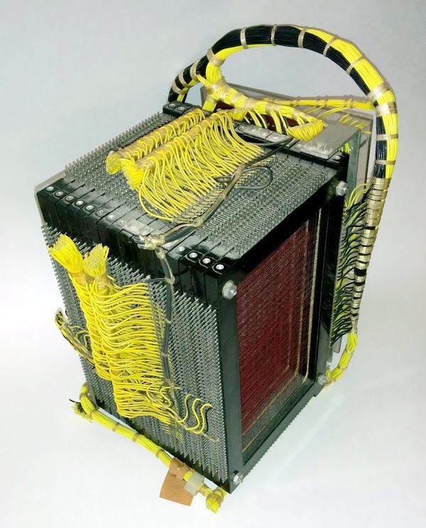 The core memory module from the IBM 1401 mainframe. The core plane at the right counts holes as part of card read validation. This plane is only partially filled with cores, strung along the red wires. The yellow wires connect the read brushes and the print hammers directly to cores.