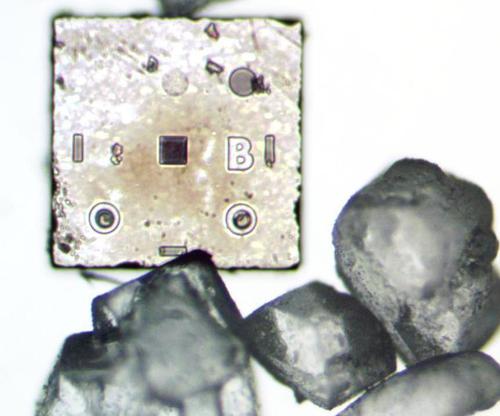 Photo of a two-diode silicon die next to sugar crystals. This photo is a composite of top-lighting to show the die details, with back-lighting to show the sugar.