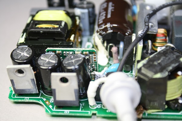 The output components in an Apple Macbook charger. The microcontroller board is visible behind the capacitors.