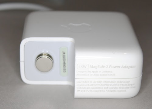 This counterfeit MagSafe 45W charger has the same 'Designed by Apple in California' text as the genuine charger. Unlike many fakes, it has a metal ground pin (although it isn't connected internally). To the right of the ground pin, the serial number label is a bit crooked, which is a hint that something isn't right.