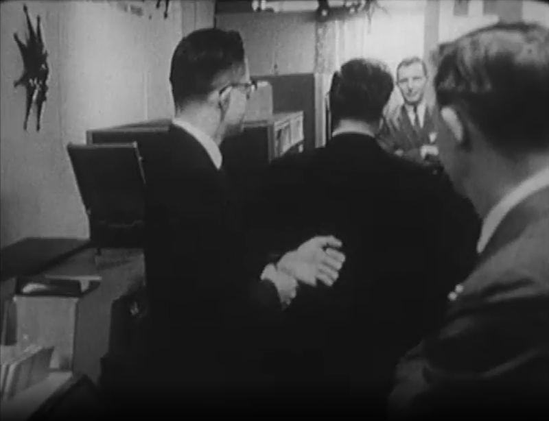 The IBM 1401 computer at Simpson's department store in 1962. The computer is barely visible behind the man's head. The 1402 card reader is at the left. Still from CBC video.