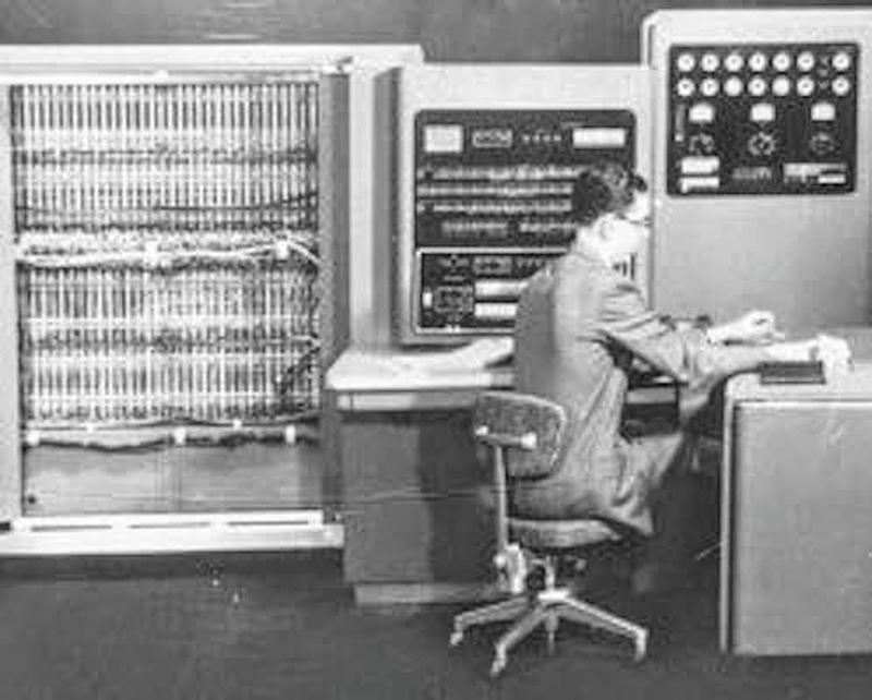 Operator at console of IBM 701. The main frame is on the left with the cover removed. The console is in the center. The power frame (with gauges) is on the right. Photo from NOAA.