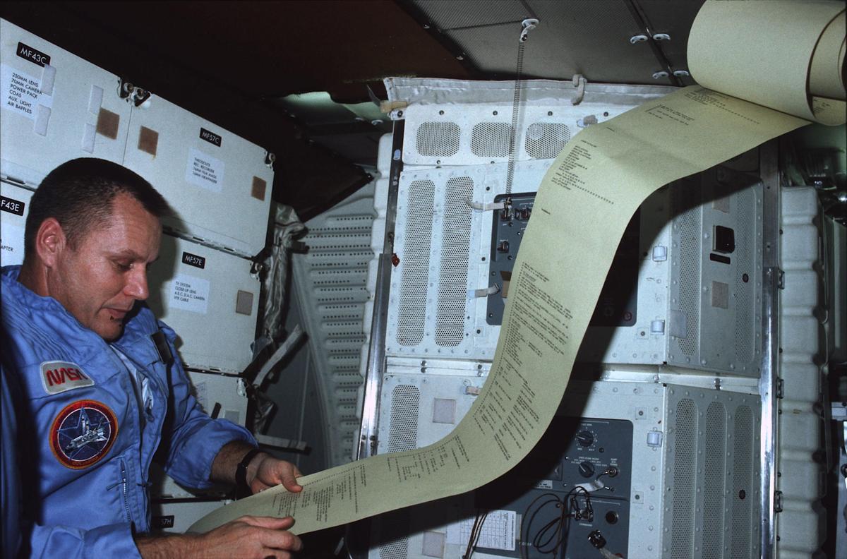 Pilot Overmyer reading a printout from the teleprinter, STS-5, November 16, 1982. From National Archives. The description says that this output is from the Text and Graphics System, but the yellow paper and the date show that this is the Interim Teleprinter.